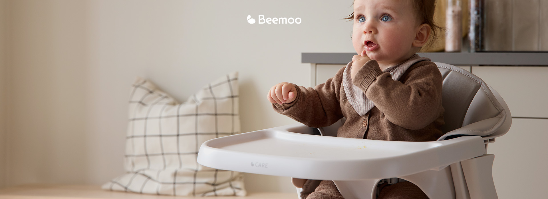 Barn sidder i højstol med teksten 'Beemoo'.